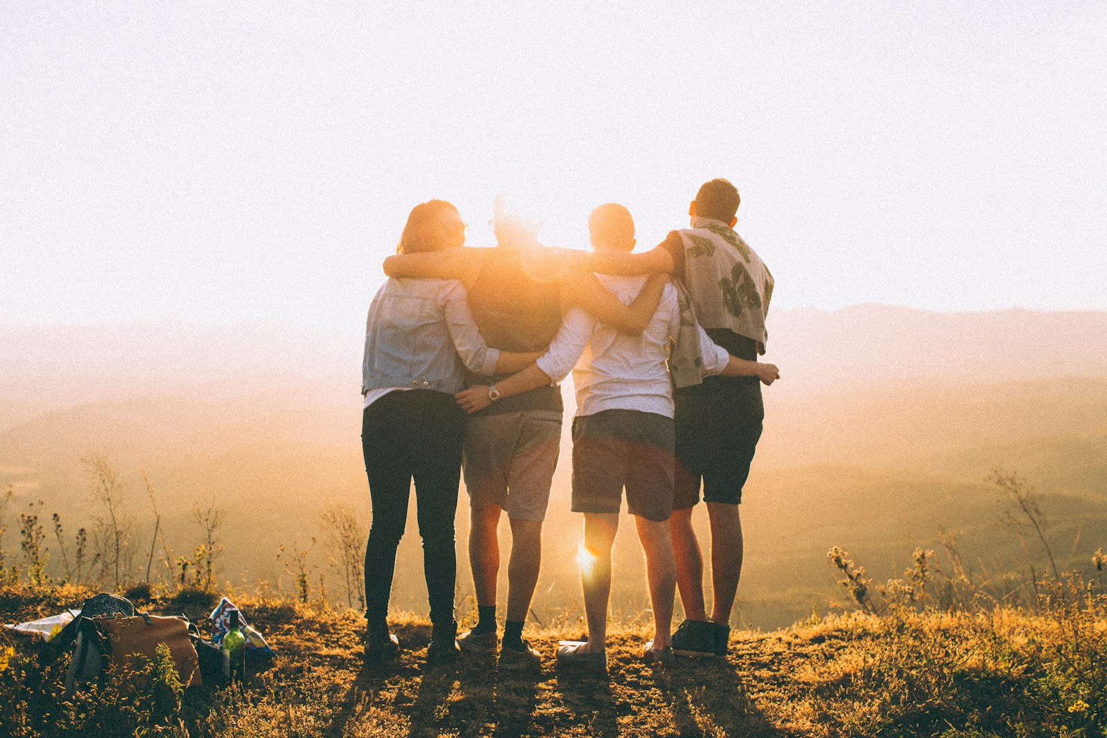 four person hands wrap around shoulders while looking at sunset, health insurance